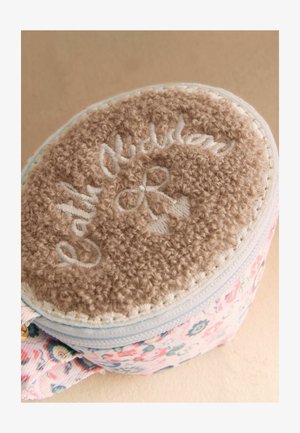 Pyöreä pussukka, jossa vaaleanruskea karvainen yläosa, jossa kirjailtu teksti "Cat & Nutmeg", ja vetoketjulla sekä kangassilmukalla varustettu kukkakuvioitu kangasrunko.