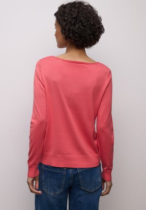 Pull corail à manches longues avec un large col, des poignets et un bas côtelés ; texture lisse et coupe décontractée, associé à un jean en denim bleu.