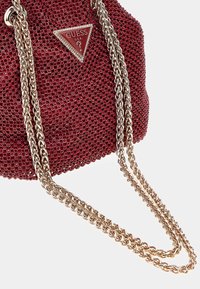 Borsa a tracolla rossa con perline, dotata di un logo Guess a forma di diamante e catene metalliche dorate, presenta una superficie testurizzata e una forma arrotondata.