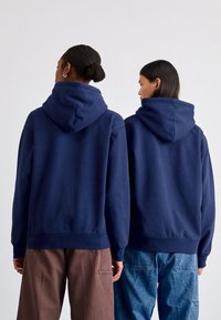 Hoodies azul-marinho com bolsos canguru e punhos elásticos, mostrados de costas em duas pessoas, apresentando um tecido macio e um corte relaxado.