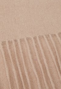 Écharpe en laine beige avec une texture douce, présentant des bords à franges et des détails cousus, affichée à plat pour mettre en valeur son design.