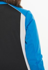 Schwarze und blaue Jacke mit weißen Akzenten. Das Design weist eine taillierte Silhouette und eine glatte Textur auf, sichtbare Nähte entlang der Nähte.