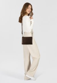 Borsa a tracolla in pelle marrone di forma rettangolare, con una tracolla rimovibile e dettagli in metallo argentato. Texture liscia.