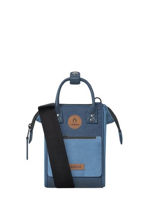 Small blue crossbody bag with front pocket, black adjustable strap, dual handles, and Cabaia brand leather patches.