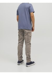 Person wearing gray cargo pants, a blue t-shirt, and navy blue sneakers standing against a plain gray background, facing away.