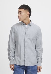 Camicia grigia chiaro con bottoni, a righe verticali, con un taschino sul petto e maniche lunghe. Realizzata in un tessuto con una sottile texture.