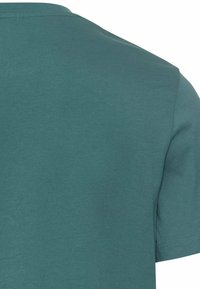 Kortærmet t-shirt i tealgrøn, lavet af blødt bomuldsstof. Har rund halsudskæring og en glat, ensartet tekstur med pæne sømme.