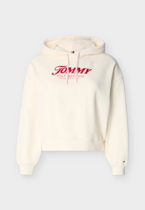 Hanorac de culoare crem cu logo roșu „Tommy Hilfiger Co.” pe față, glugă cu șnur, manșete tip rib și un mic logo în formă de steag pe manșeta mânecii stângi.