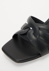 Schwarze Ledersandale mit quadratischer Zehenpartie und geflochtenen Riemen. Die Oberfläche hat eine glatte Textur und minimale Hardwaredetails.