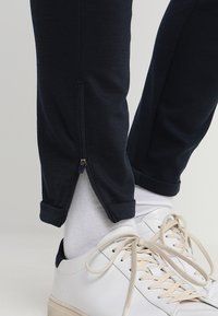 Granatowe spodnie dresowe z teksturowanej tkaniny, z suwakiem przy kostce i podwiniętymi mankietami, zestawione z białymi trampkami i skarpetkami.