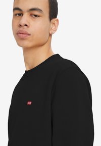 Zwarte sweatshirt van katoen, met een ronde hals en een klein rood Levi's-logo op de borst. Gladde textuur, casual pasvorm.
