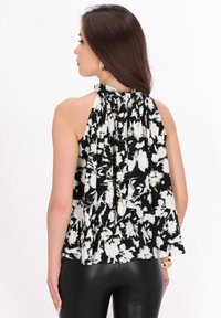 Sort og hvid ærmeløs bluse med halterneck, der har et blomstermønster og plisseret struktur, som elegant draperer bagpå.