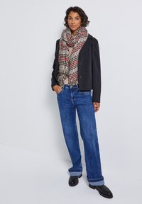 Sort cropped jakke, beige sweater, oversized ternet tørklæde i creme, rød og sort, blå brede jeans, sorte sko og naturligt hår.