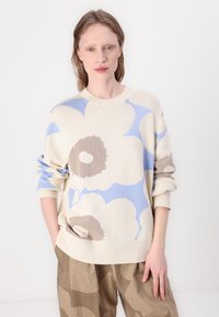 Gaišas krēmkrāsas adītas džemperis ar ziliem un brūniem ziedu rakstiem; ar apaļu kakla izgriezumu un brīvu piegriezumu. Apvienots ar brūnām biksēm ar rakstu.