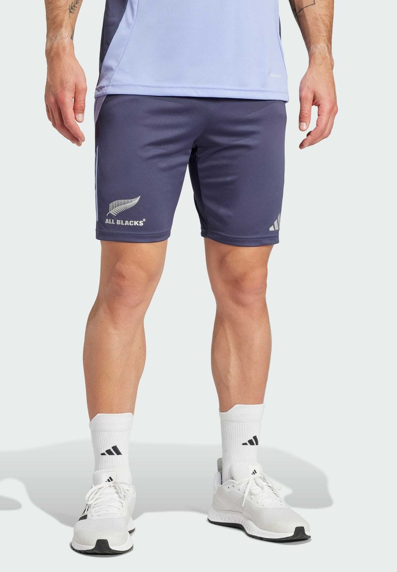 Marinefarbene Sportshorts mit "ALL BLACKS"-Logo, aus glattem Material, mit elastischem Bund und seitlichen Taschen; getragen mit weißen Socken und Schuhen.
