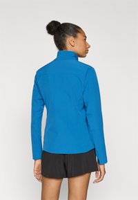 Μπλε μπουφάν με υφή, ψηλό γιακά και μακριά μανίκια. Συνδυάζεται με μαύρο σορτς, με κομψό σχέδιο.