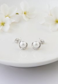 Silver studörhängen med en central pärla, omgiven av en böjd design och accentuerad med små klara stenar, placerade på en vit tallrik.