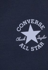 Navy fabric featuring a white circular logo with a star, text "CONVERSE," "Chuck Taylor," and "ALL STAR" in a bold font.