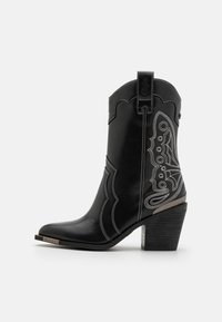 Bota de cowboy de cuero negro con costuras blancas y un diseño ornamentado en los laterales. El tacón es grueso y texturizado, con un acento metálico.