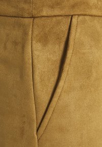 Suedetyg i en rik gyllenbrun färg har en slät struktur, med en sidficka och ren sömnad för extra detalj.