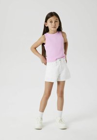 Top sans manches rose et shorts en denim blanc avec un ourlet effiloché. Des baskets blanches et des chaussettes montantes complètent la tenue. Design simple et décontracté.