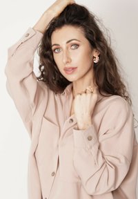 Jasnoróżowa, oversize'owa koszula z guzikami, w połączeniu z wyrazistymi kolczykami i pierścionkiem z kwiatowymi wzorami. Miękka tkanina i luźny krój.