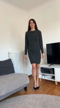 Šedé pletené šaty s dlouhými rukávy, zdobením na ramenou, přiléhavým střihem a délkou ke středu stehen, doplněné černými lodičkami na vysokém podpatku.