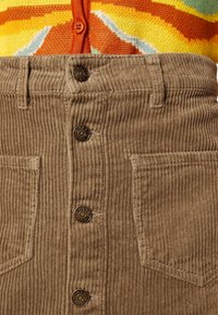 Ljusbrun kordkjol med vertikala ribbor, fem knappar, två framfickor och rak skärning.