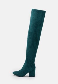 Türkise Wildleder-Stiefel bis zum Knie mit Blockabsatz und spitzer Zehe, seitlich auf einem weißen Hintergrund gezeigt.