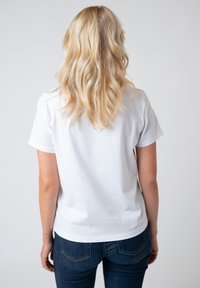 Weißes Baumwoll-T-Shirt mit kurzen Ärmeln und runder Halslinie, von hinten gezeigt, kombiniert mit dunkelblauen Jeans.