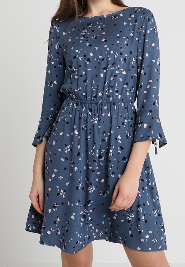 Sininen mekko, jossa on leikkisä täpläkuvio pinkillä, mustalla ja valkoisella. Mekossa on pitkät hihat, joissa on levenevät hihansuut ja elastinen vyötärö.