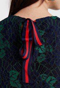 Spetsöverdel med ett blommönster i djupgrön och marinblå, med ett röd- och marinblå randigt band i midjan bak i nacken.