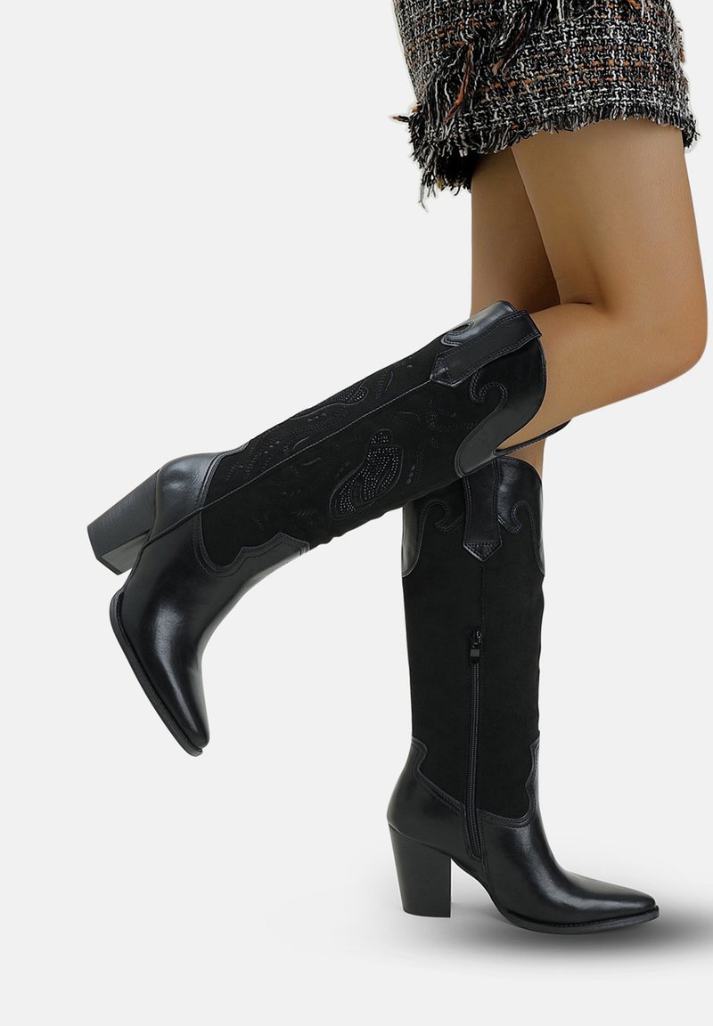 Botas negras hasta la rodilla que combinan cuero liso y ante texturizado, con punta afilada, tacón cuadrado y detalles decorativos en relieve.