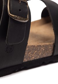 Black leather sandal with adjustable strap, cork footbed, and textured sole. Buckle details with brand logo visible.