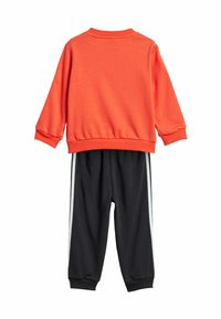 Felpa arancione con maniche lunghe, polsini e orlo a coste. Pantaloni jogger neri con strisce bianche sui lati e vita elasticizzata. Tessuto morbido.