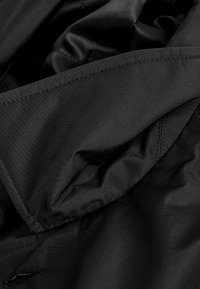 Gros plan sur un tissu noir avec des coutures visibles et des plis superposés, montrant la texture et les coutures d'un vêtement.