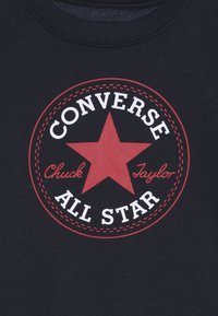 T-shirt in cotone nero con un design circolare rosso che presenta una stella centrale e il testo "Converse" e "Chuck Taylor" in bianco.