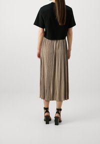 Svart kortärmad t-shirt, plisserad beige midikjol och svarta blockklackade sandaler. Slät tyg, mjuk drapering, med en strömlinjeformad silhuett.