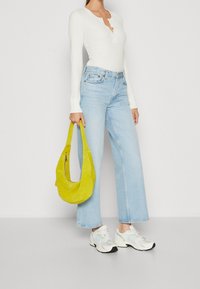 Vit ribbade långärmade topp med henley-krage, ljusblå vida jeans och en gul mockaväska över axeln. Vita sneakers med detaljer.