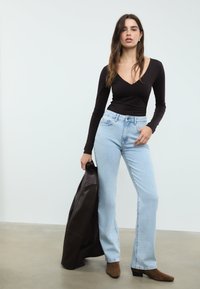 Crna bluza dugih rukava s V-izrezom, svijetloplave traperice visokog struka s širim nogavicama, smeđe čizmice s petom i tamnosmeđa kožna jakna.