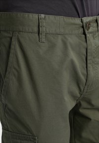 Olivgröna cargobyxor med knappstängning, bältesöppningar och flera fickor. Tillverkade av lätt, texturerad tyg.