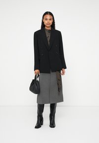 Blazer nere a doppio petto, top trasparente marrone con motivo a foglie, gonna midi grigia, stivali neri fino al ginocchio e una piccola borsa nera arricciata.