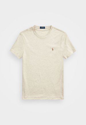 T-shirt de algodão bege com gola redonda, mangas curtas e um pequeno logótipo bordado no lado esquerdo do peito. Textura suave e design clássico.