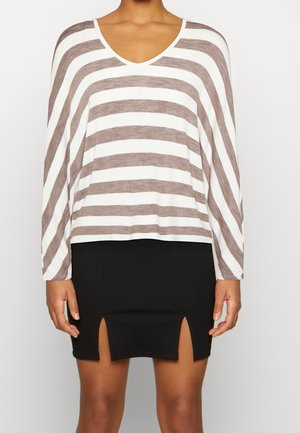 Top à manches longues blanc avec des rayures horizontales marron, doté d'un décolleté en V ; associé à une mini jupe noire avec des fentes sur les côtés.