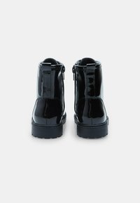 Botines de charol negro con un acabado suave, que cuentan con una cremallera lateral, punta redonda y suela negra resistente.