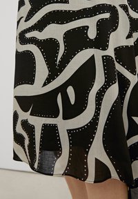 Zwart en roomkleurig jurk met abstracte, vloeiende patronen en gestippelde accenten, met een lichtgewicht, gedrapeerde textuur. De zoom is gebogen.