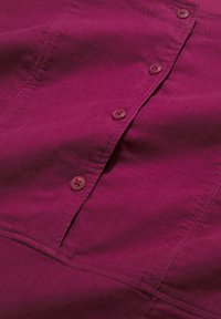 Fukšijas krāsas korduroja audums ar pogu rāvējslēdzēju, kas ietver apaļas, nedaudz spīdīgas pogas un ribotu tekstūru.