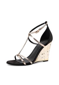 Sandalo con zeppa nera e accenti in oro metallico. Presenta cinturini incrociati e un tacco a zeppa geometrico texture. Materiali scamosciati e lisci.