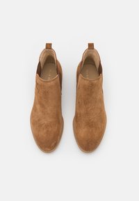 Bruine suède enkellaarzen met elastische zijpanelen, ronde neus en een trekband. Gladde textuur met gestikte details langs de zool.