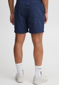 Granatowe teksturowane szorty z elastycznym pasem i tylną kieszenią, zestawione z białymi skarpetkami do kostek i szarymi trampkami.